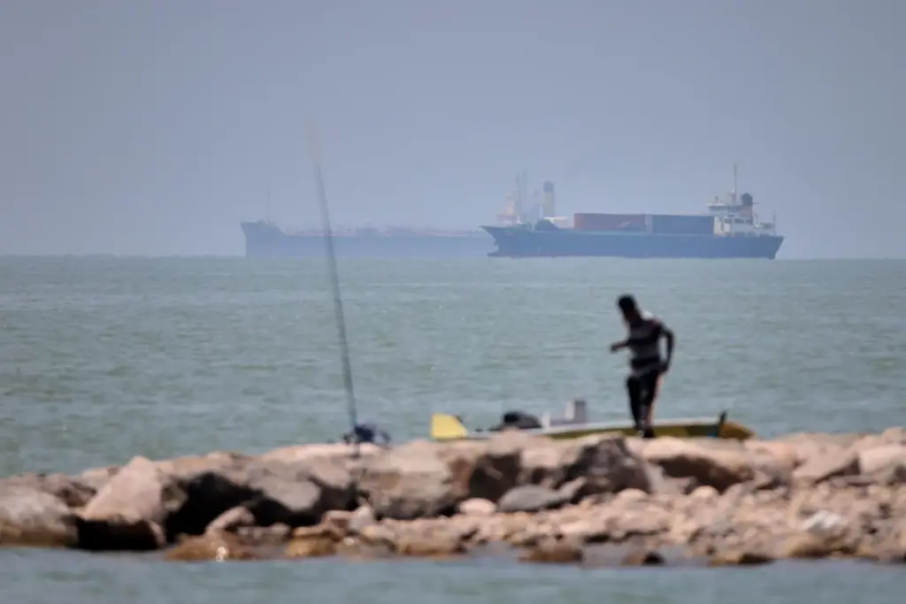 A man stands beside a fishing pole along the shore of the Strait of Hormuz.