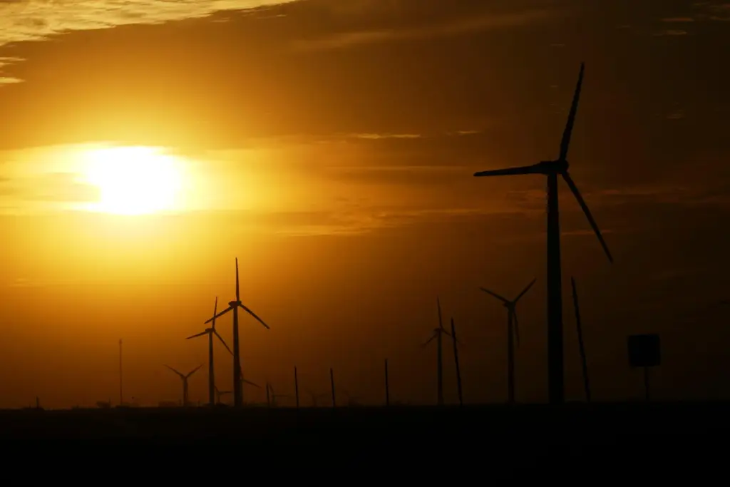 FILE – Wind turbines are visible as the sun begins...