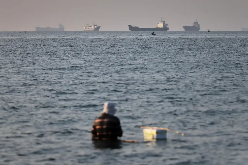 A person sits on shallow water as cargo and commercial...