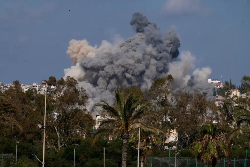 People swim on a public beach as smoke rises from an Israeli airstrike.