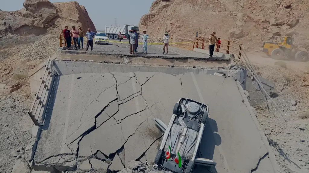 An overturned car sits on a section of a destroyed bridge.