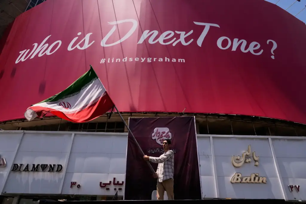 A man waves an Iranian flag beneath a billboard reading, 