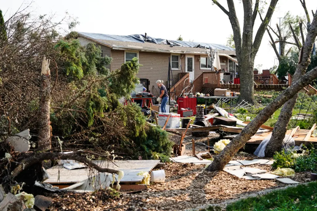 People clean up debris in front of a damaged home...