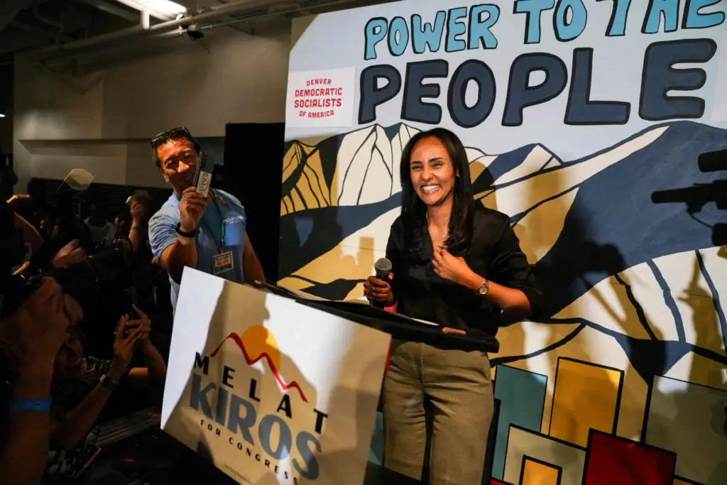 Democratic congressional candidate Melat Kiros stands on stage as supporters cheer.