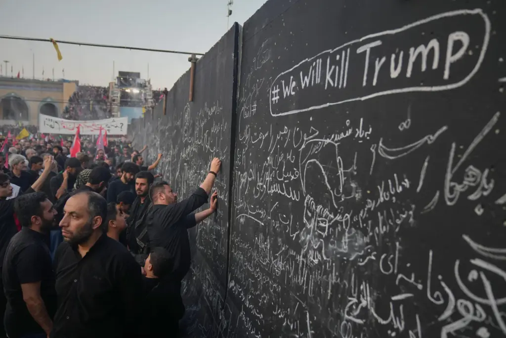 Mourners write messages on a wall, including one in English that reads 