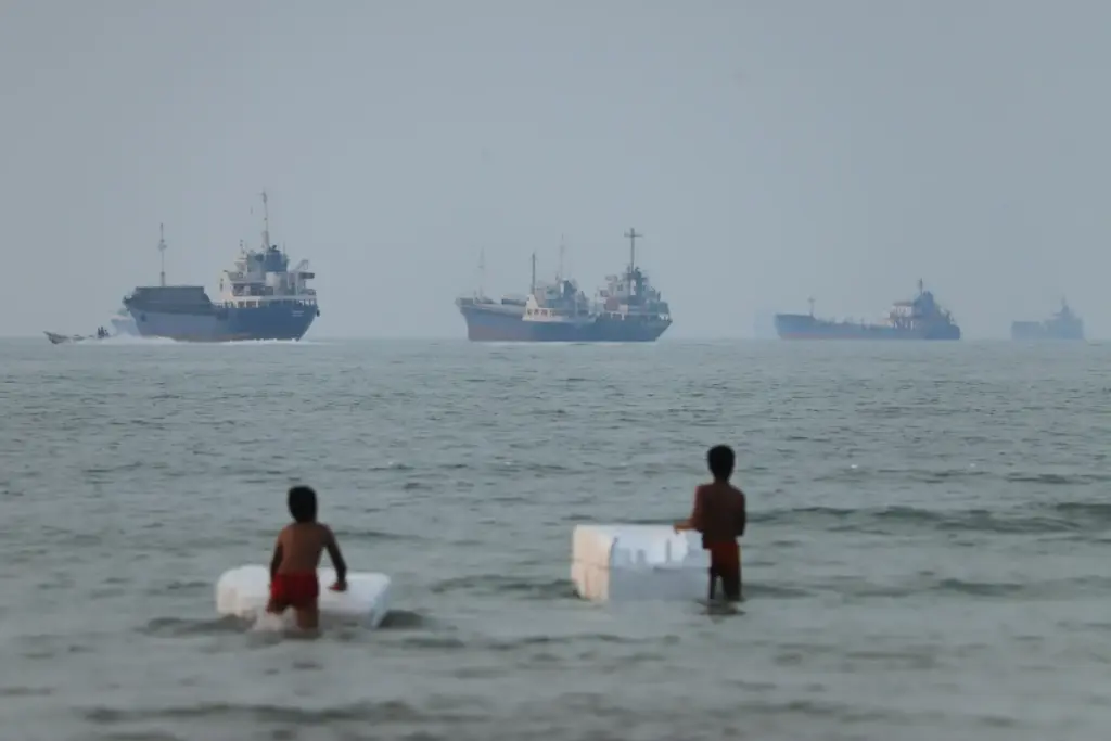 Two boys stand in shallow water with foam floats as...