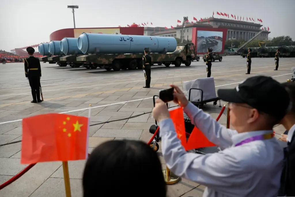 Spectators wave Chinese flags as military vehicles carrying JL-2 submarine-launched missiles roll during a parade.