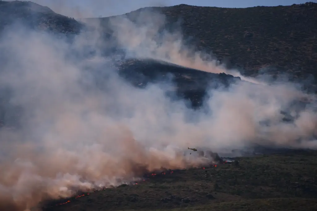 A firefighting helicopter drops water on the flames as a...