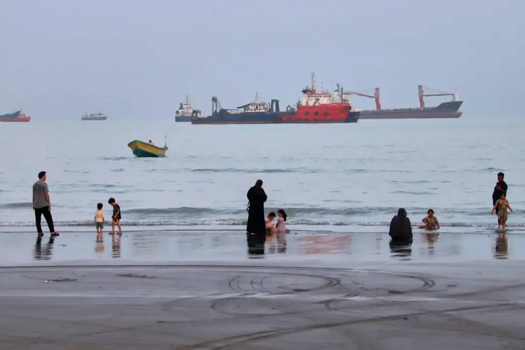 People spend time at a beach as commercial vessels are anchored in the Strait of Hormuz.