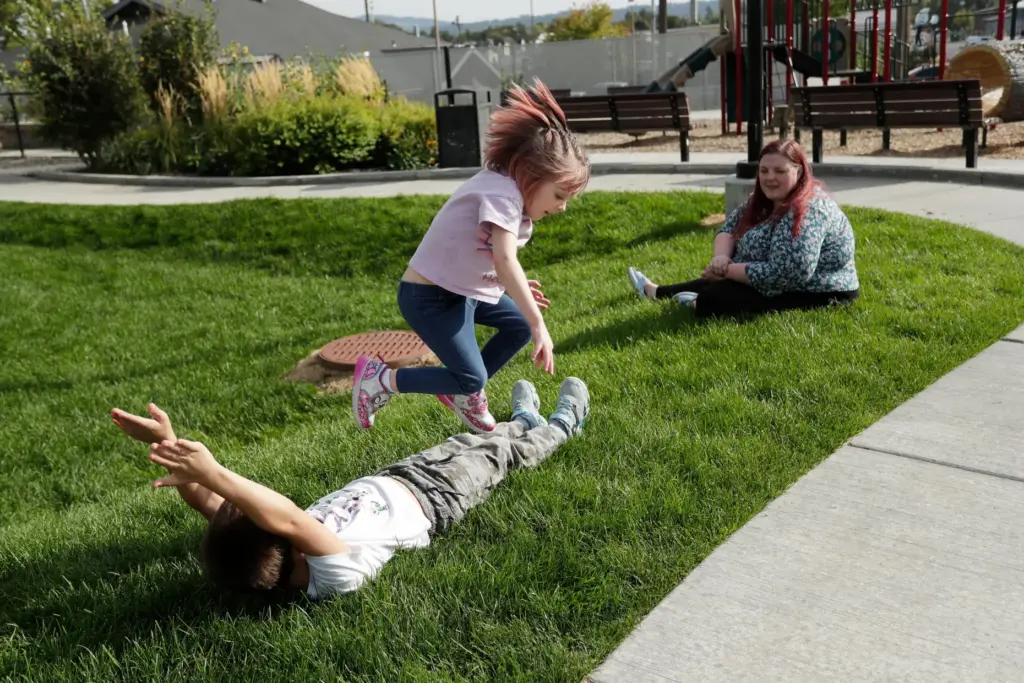 Evie Reed, center, jumps over her brother Kian Reed, left,...