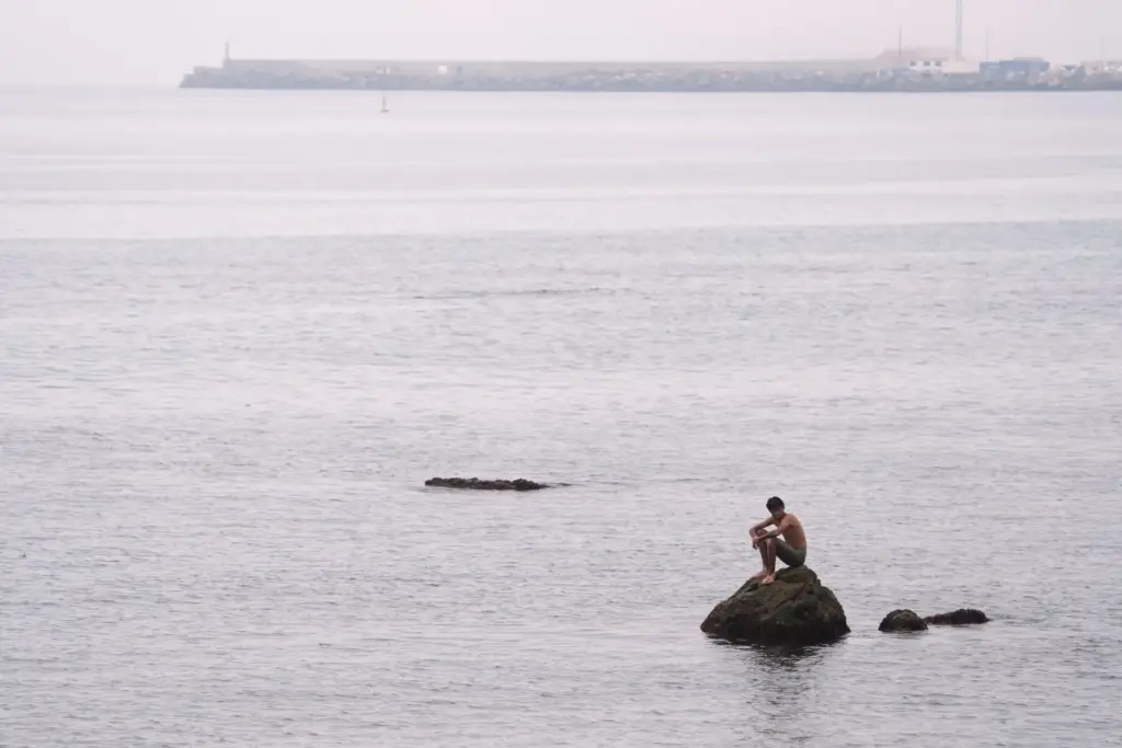 A migrant sits on a rock at El Trampolín beach...