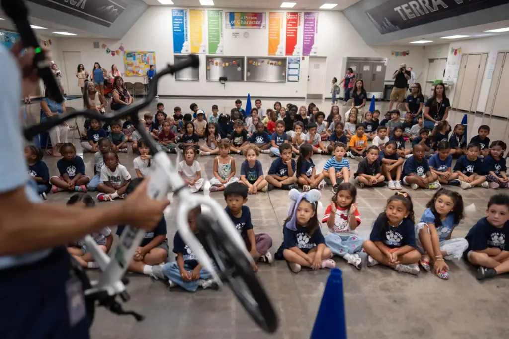 Physical education teacher Ray Herrera demonstrates how to ride a bike as students watch.