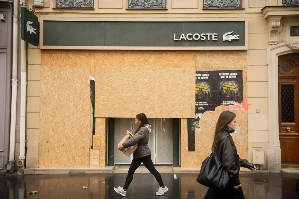 Passersby walk past a boarded-up store on the eve of...
