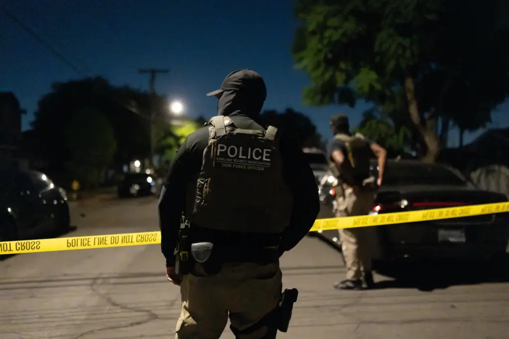 A Homeland Security Investigations task force officer stands near police tape.